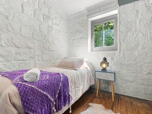 A bedroom with a bed, a nightstand, a window, and a textured wall. - Oceana Suites San Jose de Maipo (San Jose de Maipo)