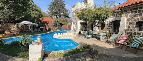 Una piscina con sillas de descanso, un edificio de piedra y un patio cubierto.