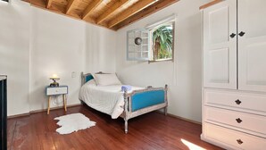 Ein Schlafzimmer mit Holzboden, einem Bett mit blauer Kopfteil, einer weißen Kommode und einem kleinen Nachttisch mit Lampe.