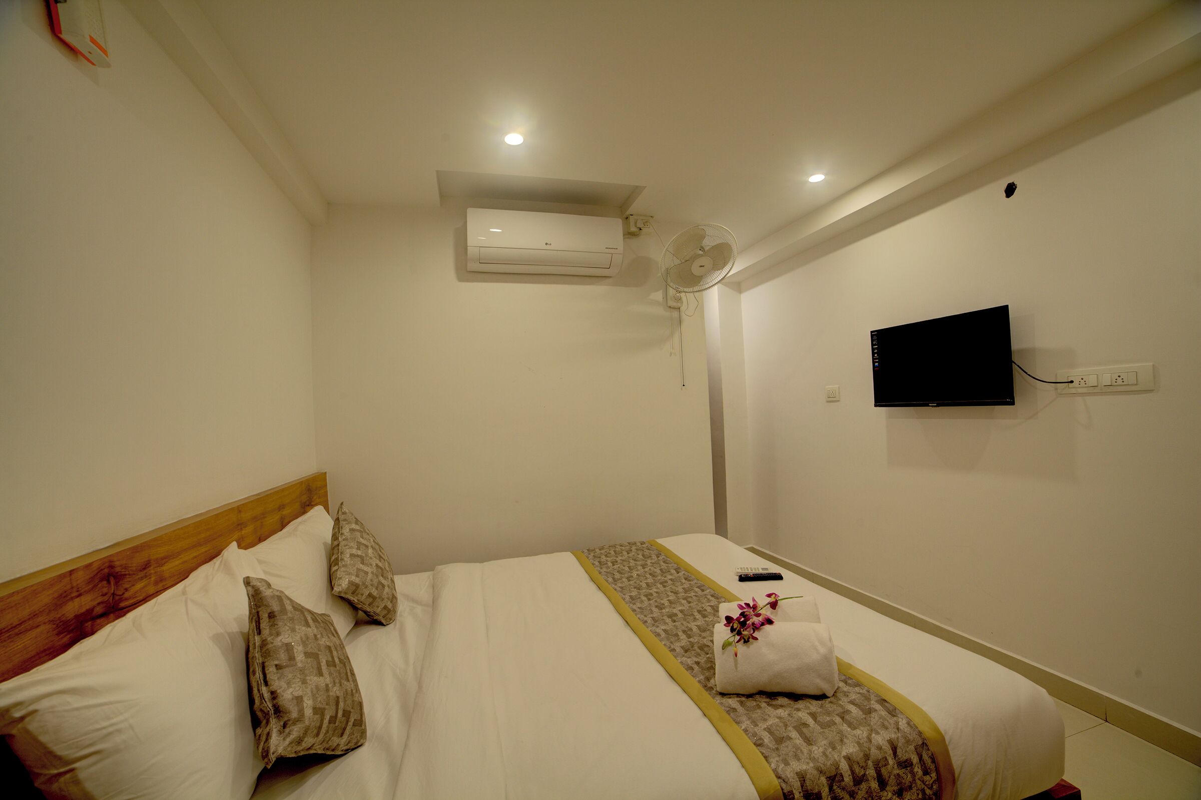 Una habitación de hotel con cama, almohadas, un control remoto, televisor y aire acondicionado.