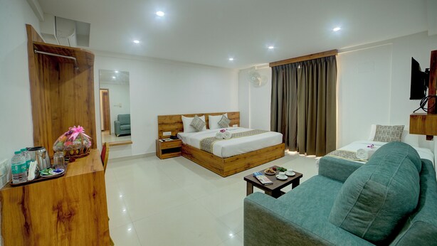 A hotel room with a wooden bed, a grey sofa, a wooden desk with toiletries, and a TV on the wall. - Fly Inn Bangalore Airport (Begur)