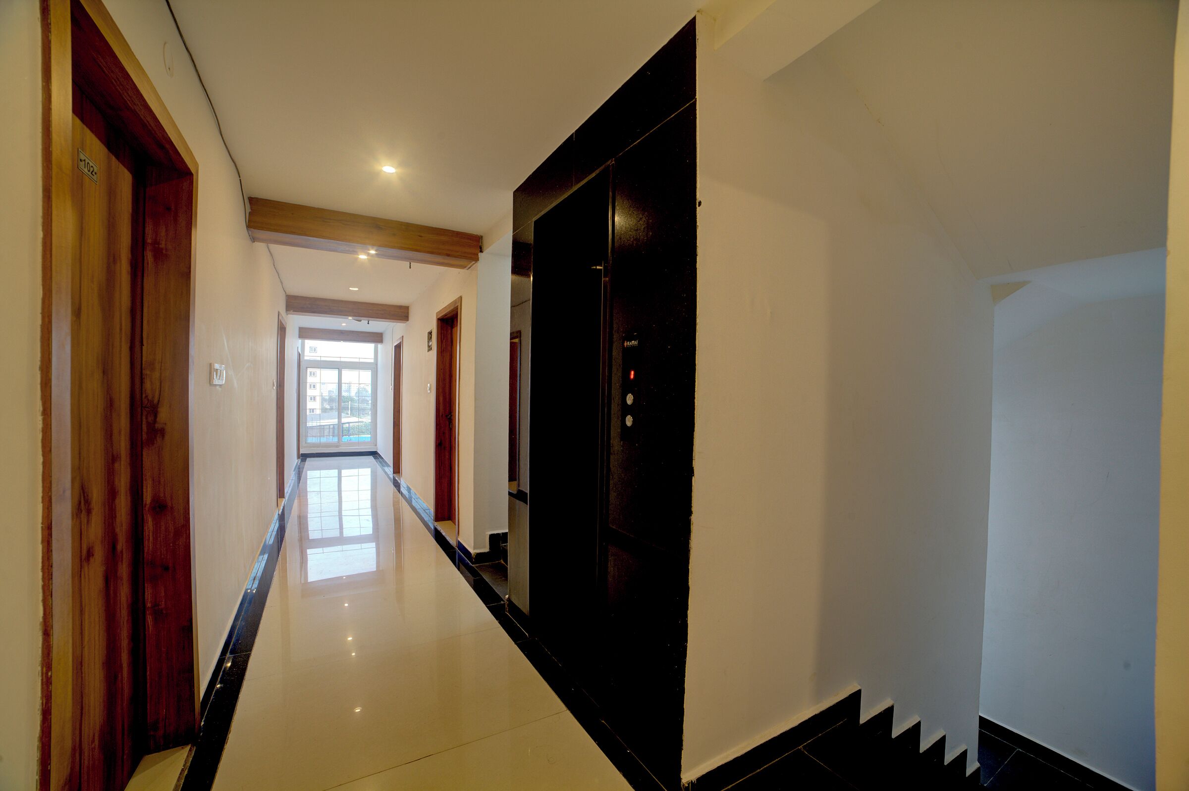 Un pasillo con piso pulido, puertas de madera y una puerta negra que da a una habitación.