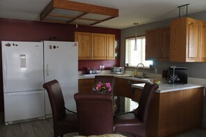 A compact kitchen with wooden cabinets, a white refrigerator, a dining table with chairs, and a small island with a sink.