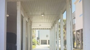 Un couloir extérieur couvert, doté d’un sol en béton et de piliers blancs, qui mène à un bâtiment à toit plat.