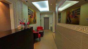 A hallway with a reception desk, red chairs, and artwork on the walls. - Hotel Farid (Dakar)