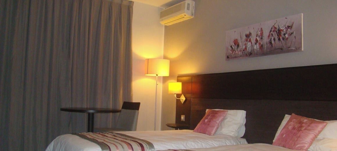 A hotel room with a bed, a desk, a lamp, and a painting on the wall.