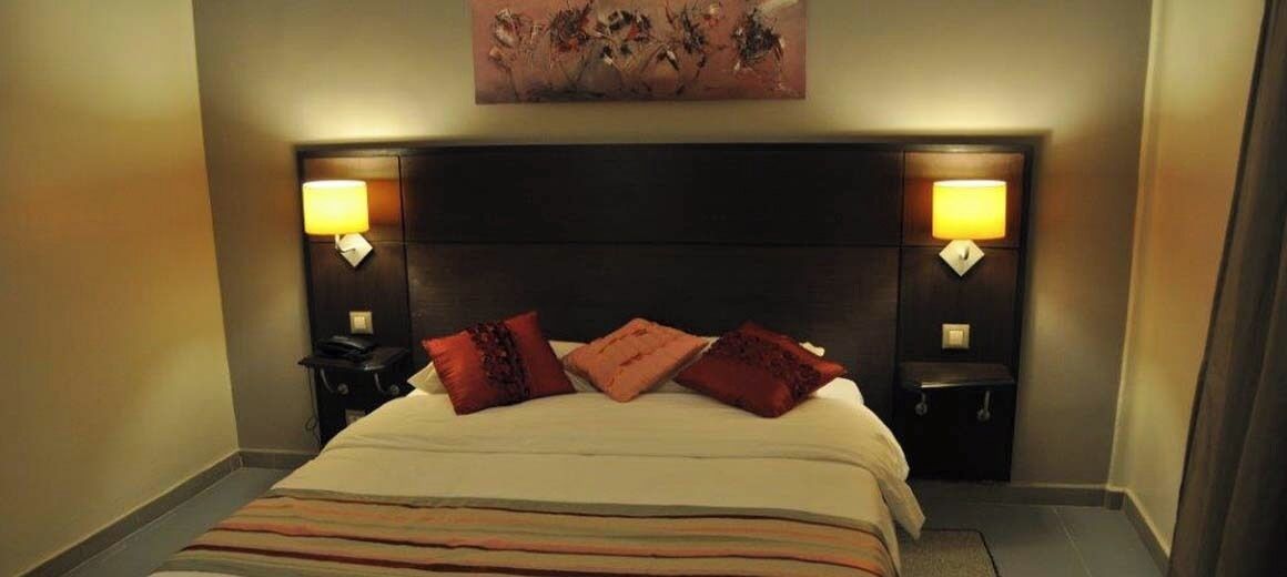 A hotel room with a bed, two bedside tables, lamps, and a painting on the wall.
