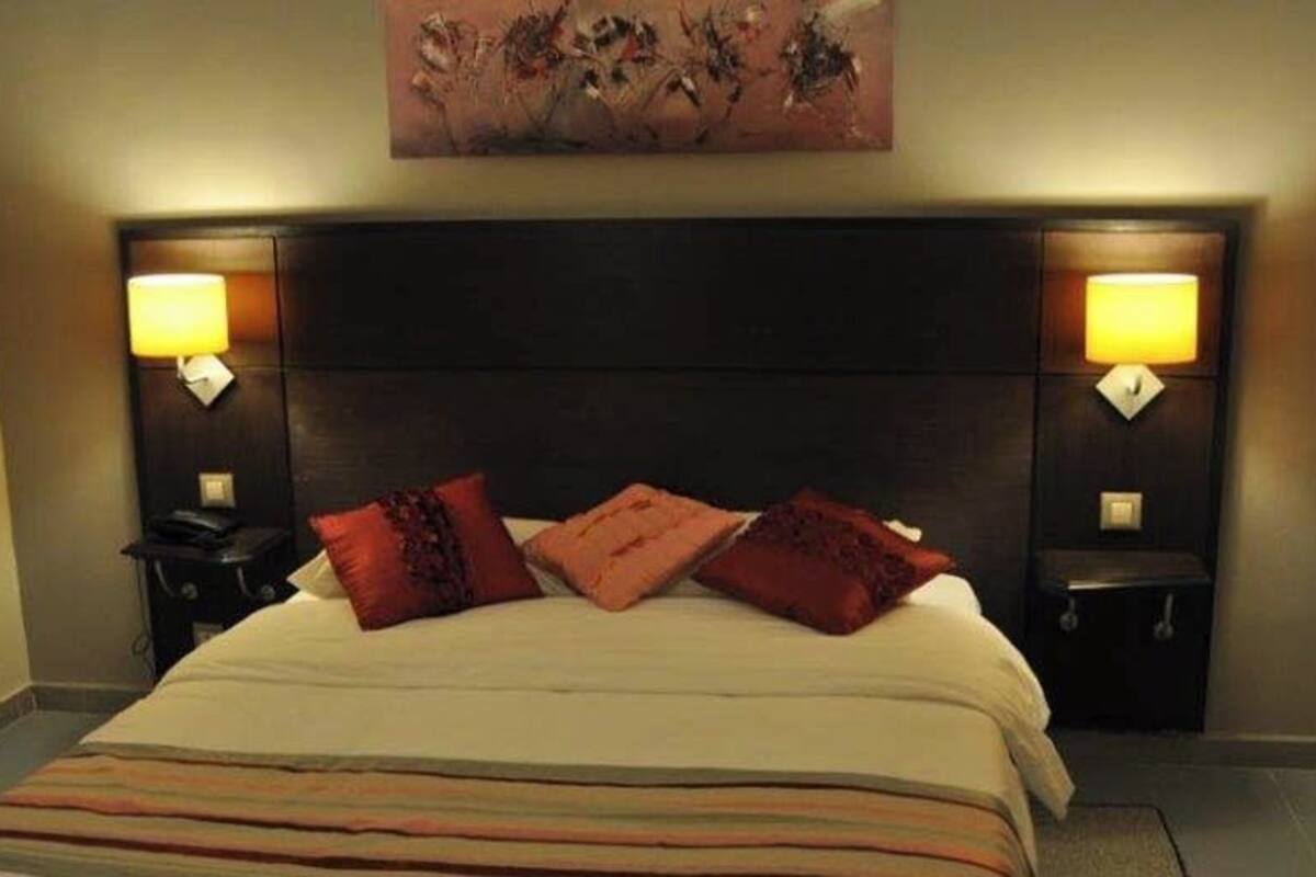 Una habitación de hotel con una cama, dos mesitas de noche, lámparas y un cuadro en la pared.