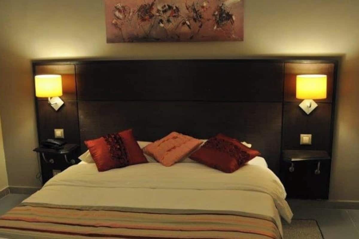A hotel room with a bed, two bedside tables, lamps, and a painting on the wall.