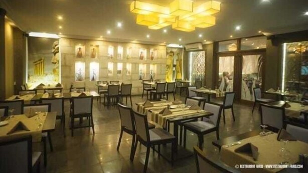 A restaurant with multiple tables and chairs, a modern chandelier, and artwork on the walls. - Hotel Farid (Dakar)
