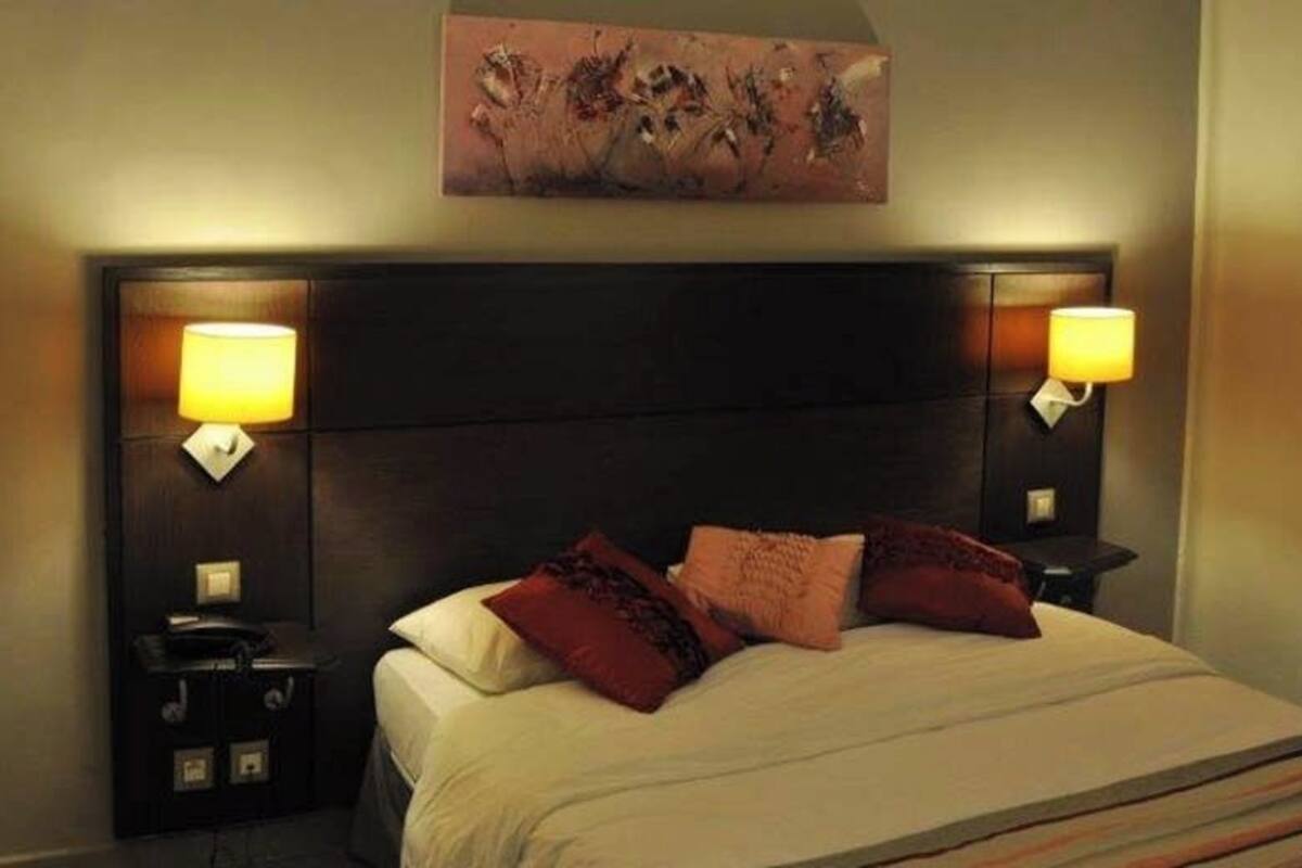 Habitación de hotel con una cama grande, dos mesitas de noche, cabecera y una obra de arte colgada en la pared.