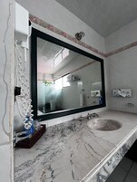A bathroom with a large mirror, a sink, and a shower area.