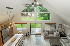 Amplio loft con comedor, cocina y zona de estar, con ventanas grandes que ofrecen vistas a un área boscosa.
