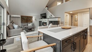 A modern kitchen with a central island, a dining area with chairs, a sofa, and a fireplace. - Luxury Golf Course Retreat – Sun Country, Cle Elum – Sleeps 8 (Cle Elum)