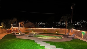 Un patio trasero bien iluminado con una zona de estar circular, una piscina pequeña y una escalera de piedra que lleva a un patio.