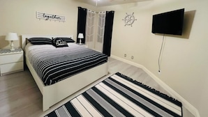 Un dormitorio con cama, ventilador de techo, televisor montado en la pared y ventana con cortinas.
