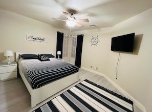 A bedroom with a bed, a ceiling fan, a TV mounted on the wall, and a window with curtains. - Spacious 4-bedroom house in tranquil Desert Hot Springs with AC (Desert Hot Springs)