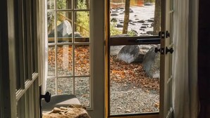 A wooden door with a glass panel leading to a view of a river, rocks, and autumn foliage. - Warner's Camp Riverfront Retreat: Cabins, Hot Tub, Saunas, Swimming Hole (Upper Jay)
