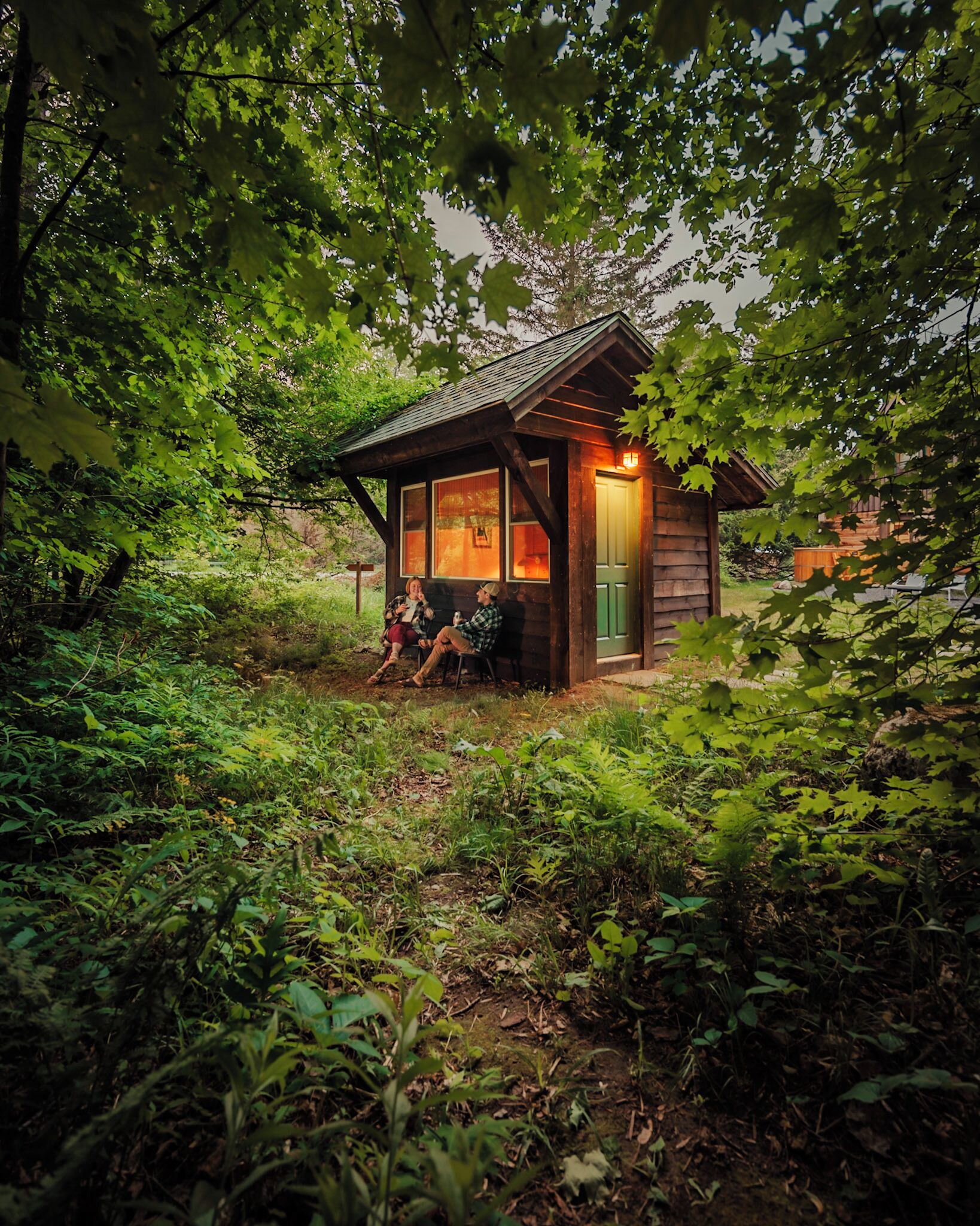A rustic cabin with a porch, surrounded by dense greenery.