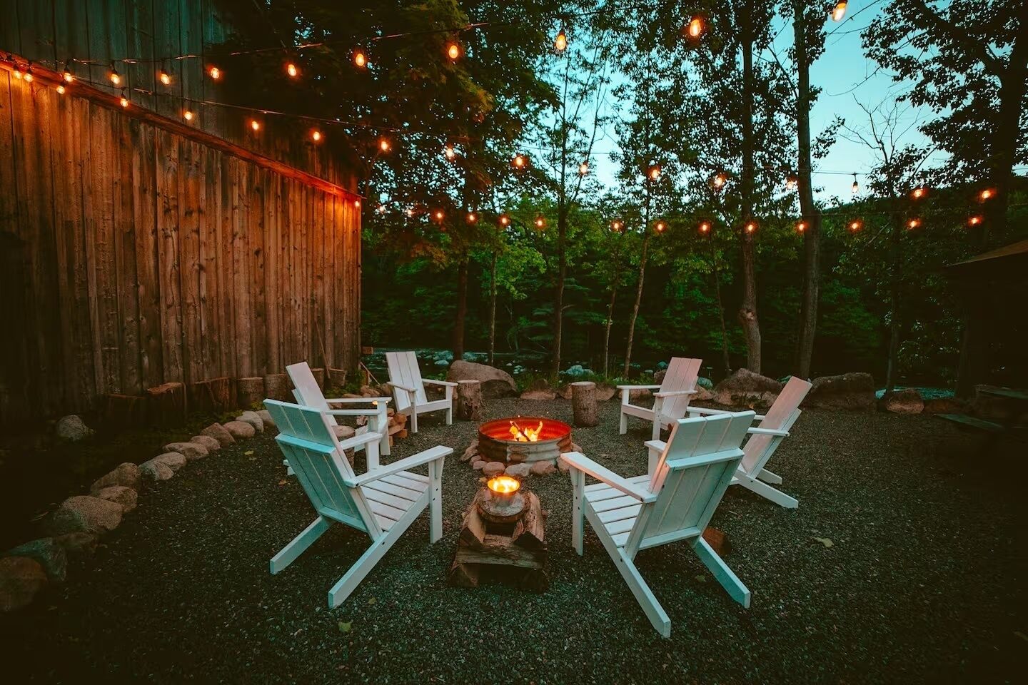 Un foyer entouré de fauteuils Adirondack, dans un cadre extérieur boisé.