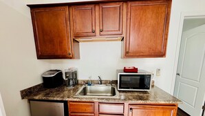 A compact kitchen with wooden cabinets, a stainless steel sink, a toaster, a coffee maker, and a microwave. - The Starland Loft Apartment- Savannah, GA (Savannah)