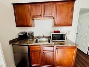 A compact kitchen with wooden cabinets, a stainless steel sink, a toaster, a coffee maker, and a microwave. - The Starland Loft Apartment- Savannah, GA (Savannah)