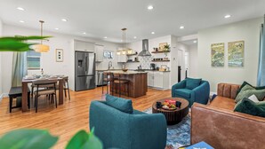 A modern kitchen with white cabinets, a stainless steel refrigerator, and a central island. There are two teal sofas and a brown leather couch in the living area. - New- Encore Retreat- Sauna-Fire Pit- Theater Room (Colorado Springs)