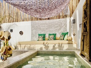 Ein Poolbereich mit einer Holzbank, grünen Kissen und einer gemusterten Decke.