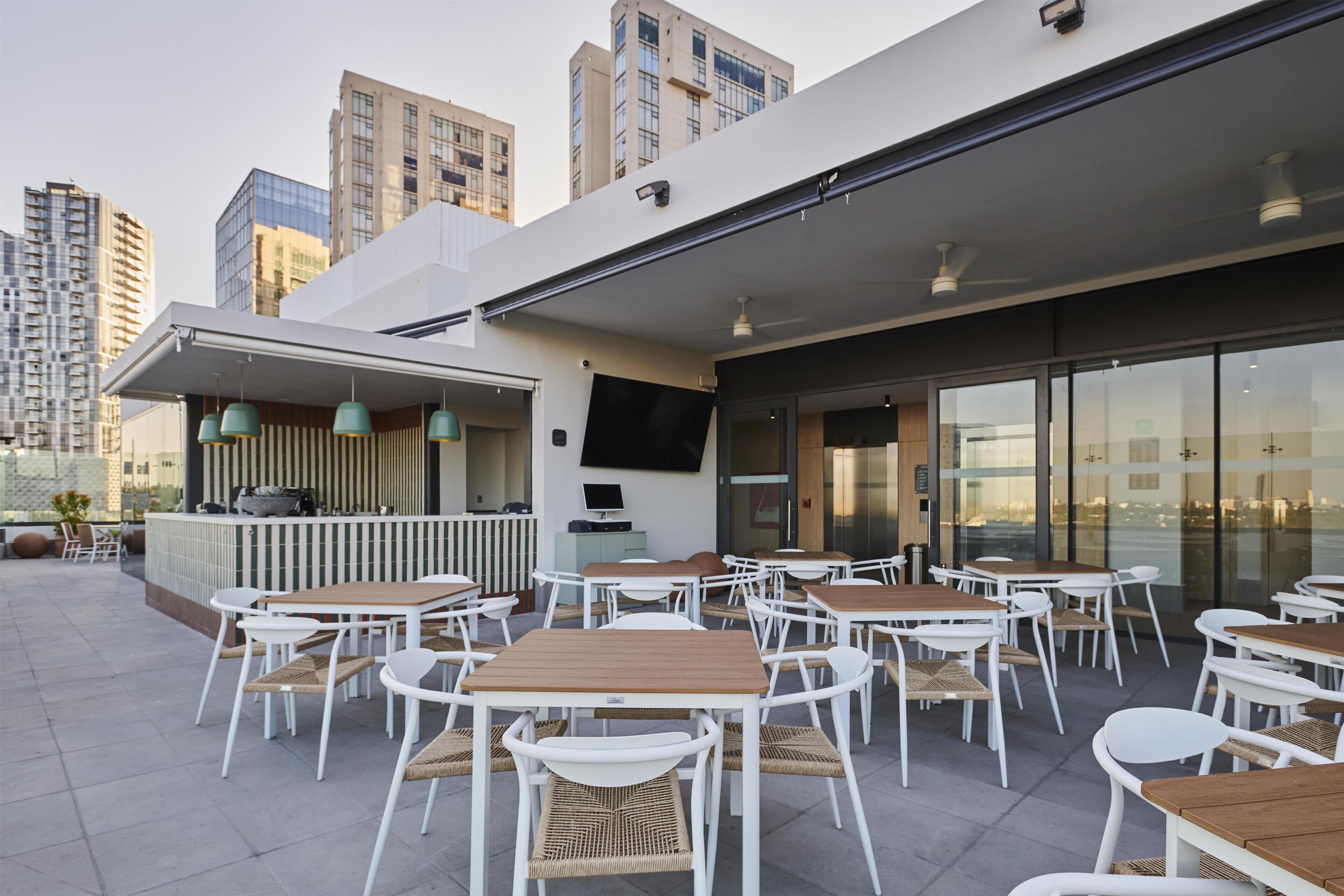 Ein Außenbereich mit Terrasse, mehreren Tischen und Stühlen, einer Bar und einem Fernsehbildschirm.