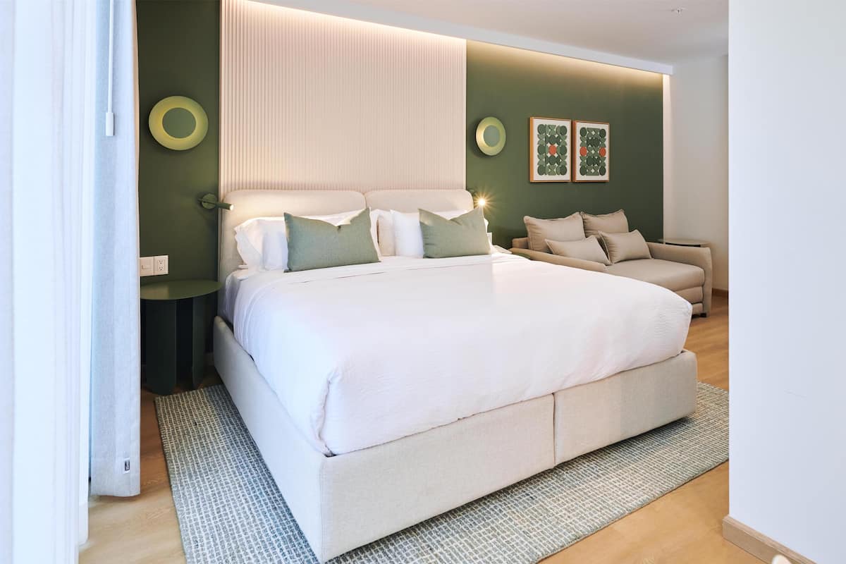 Um quarto moderno com uma cama grande, um sofá e uma parede verde como destaque.