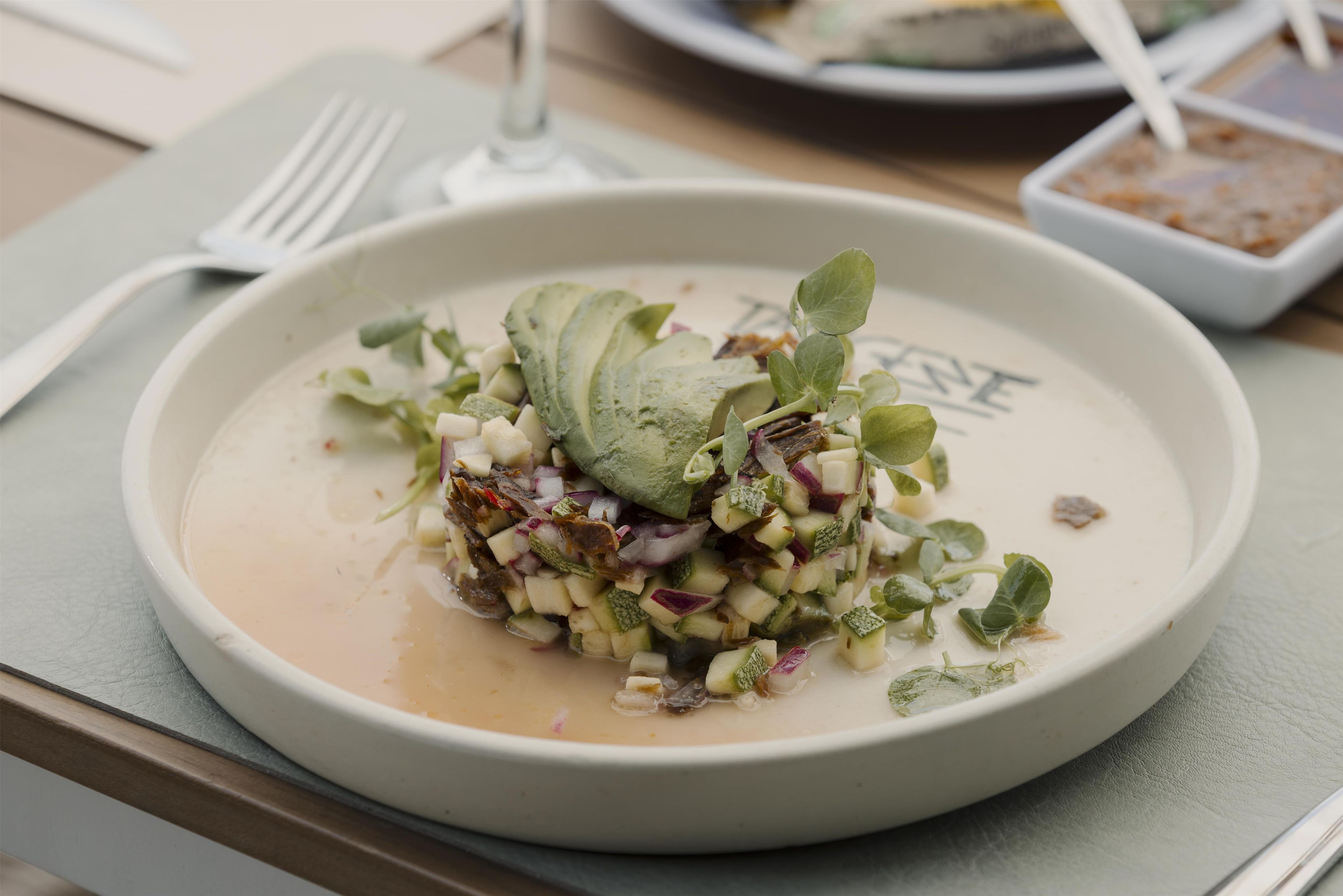 A plate of food with a creamy base, topped with green leaves, diced vegetables, and a garnish.