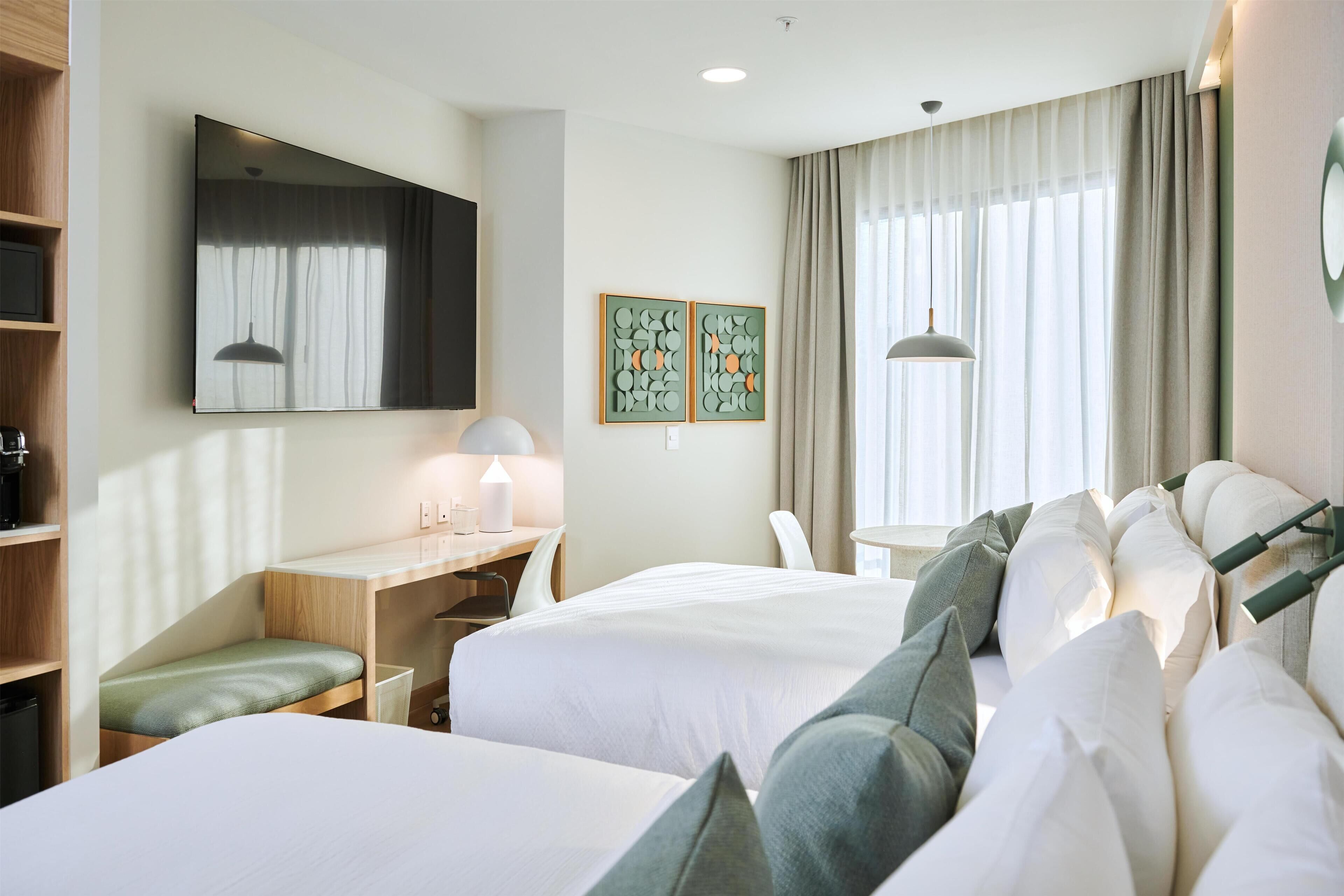 A hotel room with two beds, a desk, a chair, a small table, and a large window with curtains.