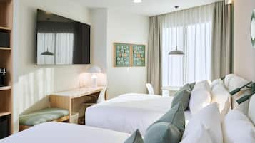 Habitación de hotel con dos camas, un escritorio, una silla, una mesita y un amplio ventanal con cortinas.