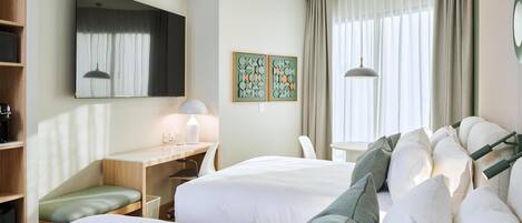 A hotel room with two beds, a desk, a chair, a small table, and a large window with curtains.