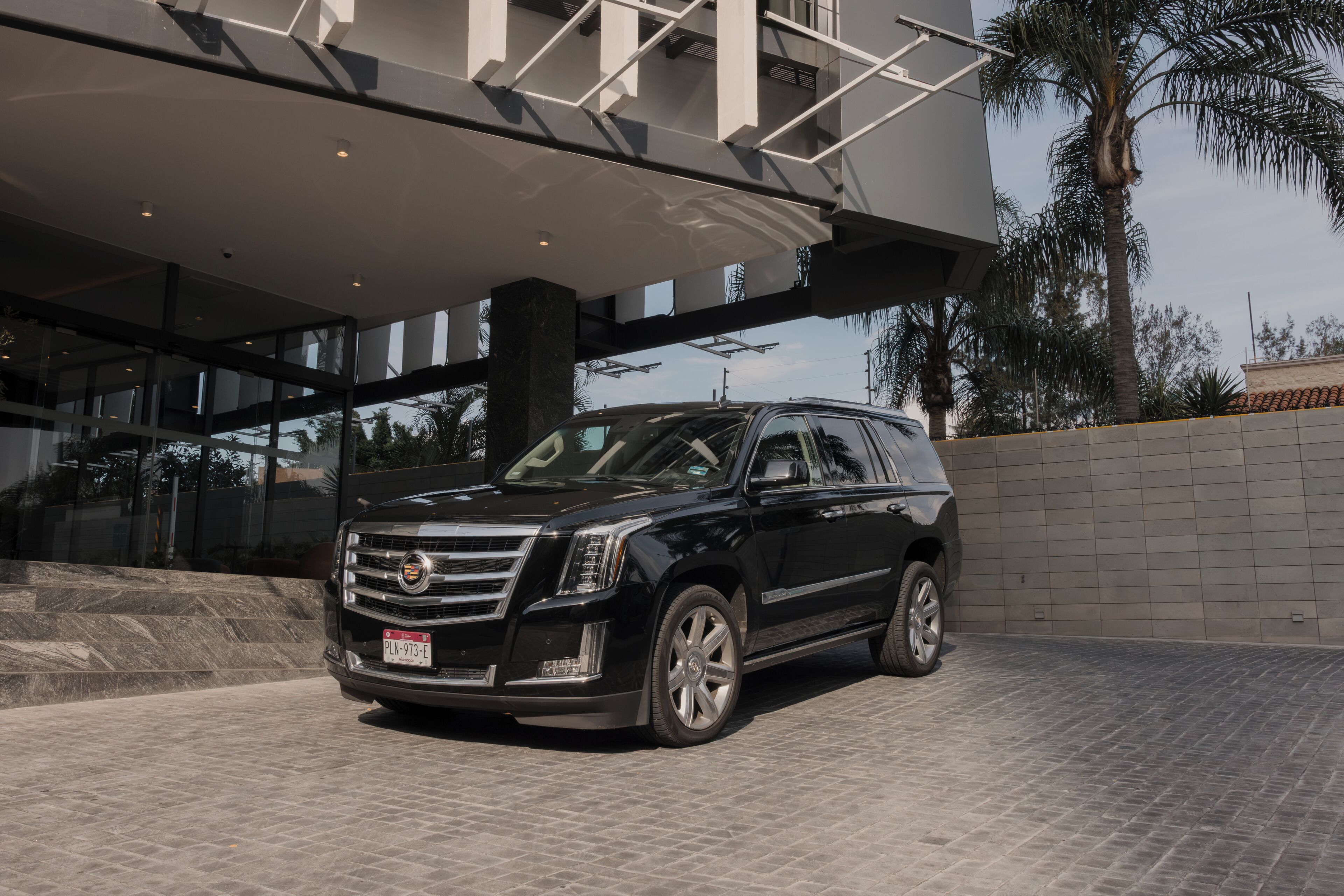 Een zwarte Cadillac SUV geparkeerd voor een modern gebouw met grote ramen en een bakstenen muur.