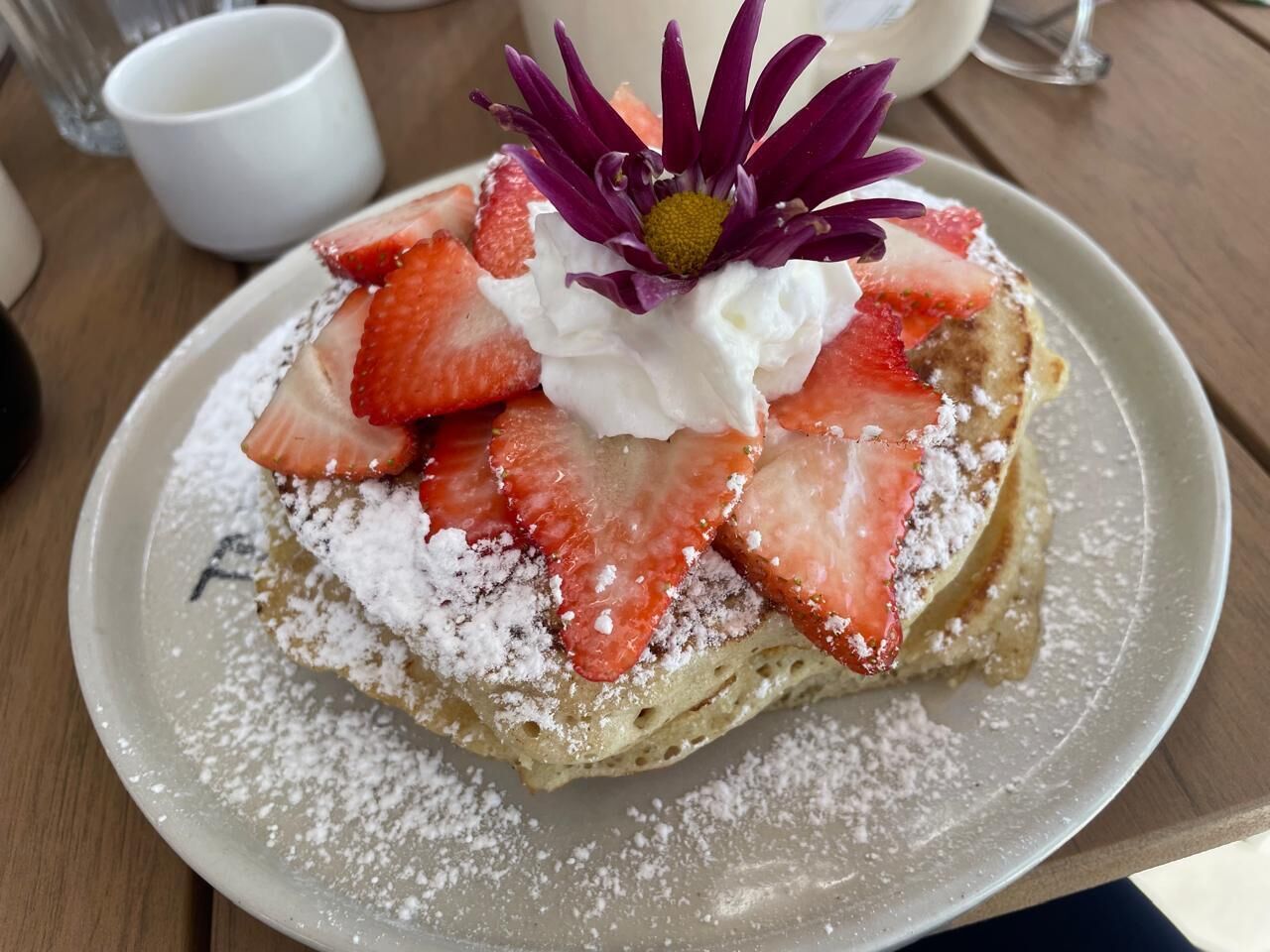 Un plato con un postre cubierto de fresas, crema batida y una flor morada.