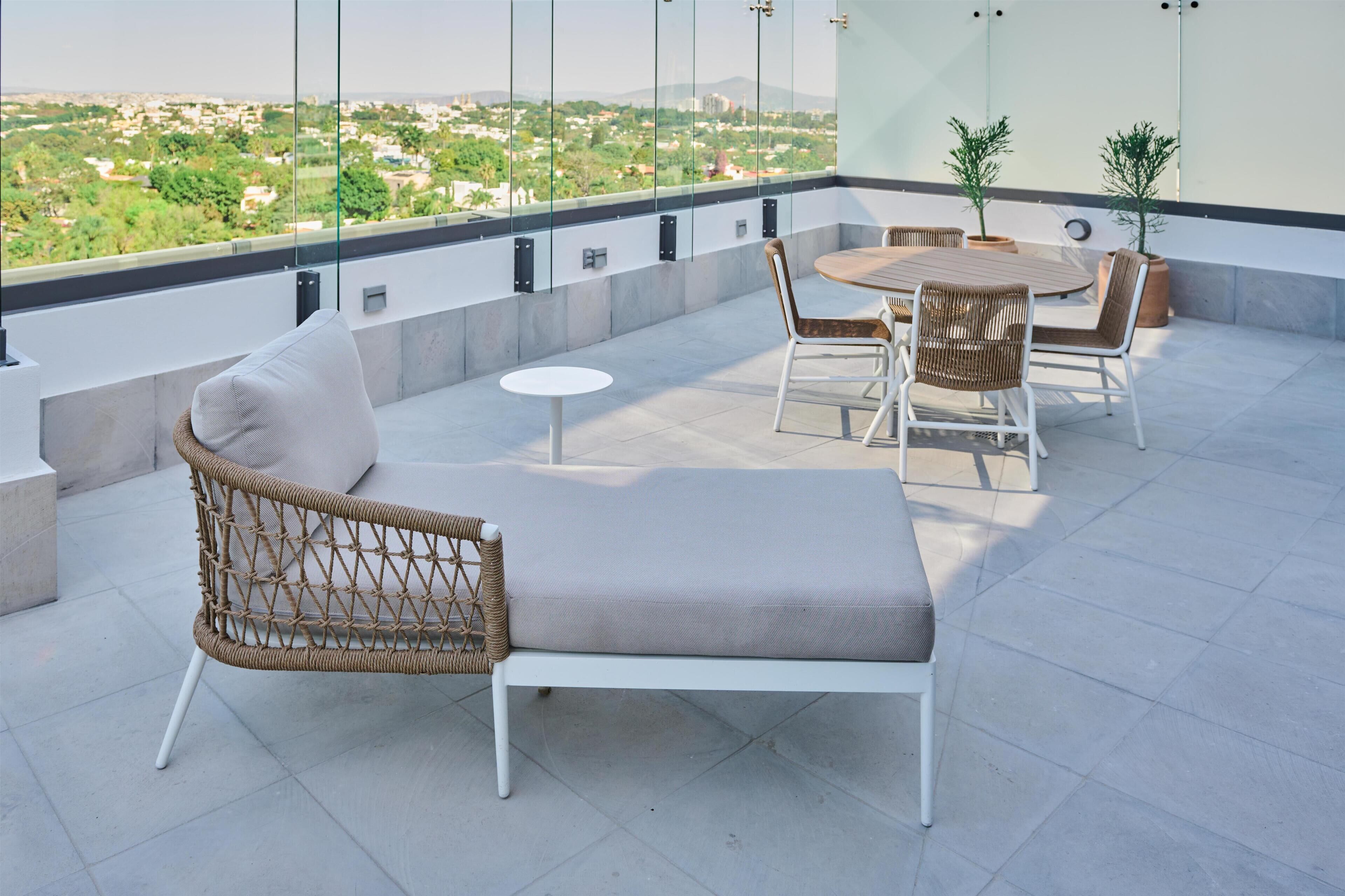 Una terraza en la azotea con una silla de mimbre, una mesa redonda y dos macetas.