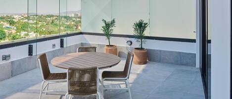 Una terraza en la azotea con una mesa redonda y sillas, dos plantas en macetas y vistas de un paisaje urbano.