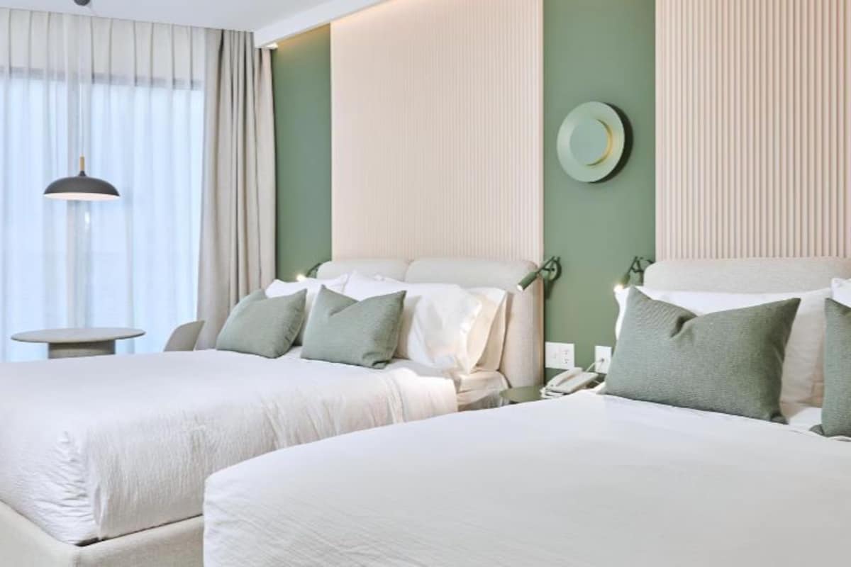Ein Hotelzimmer mit zwei Betten, einem Nachttisch, einer Lampe und einem an der Wand befestigten Telefon.