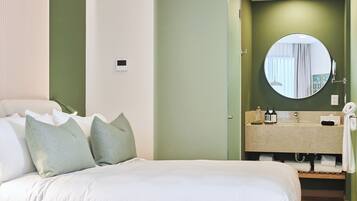 Une chambre d’hôtel avec un lit, des oreillers, un miroir rond, un lavabo et un porte-serviettes.
