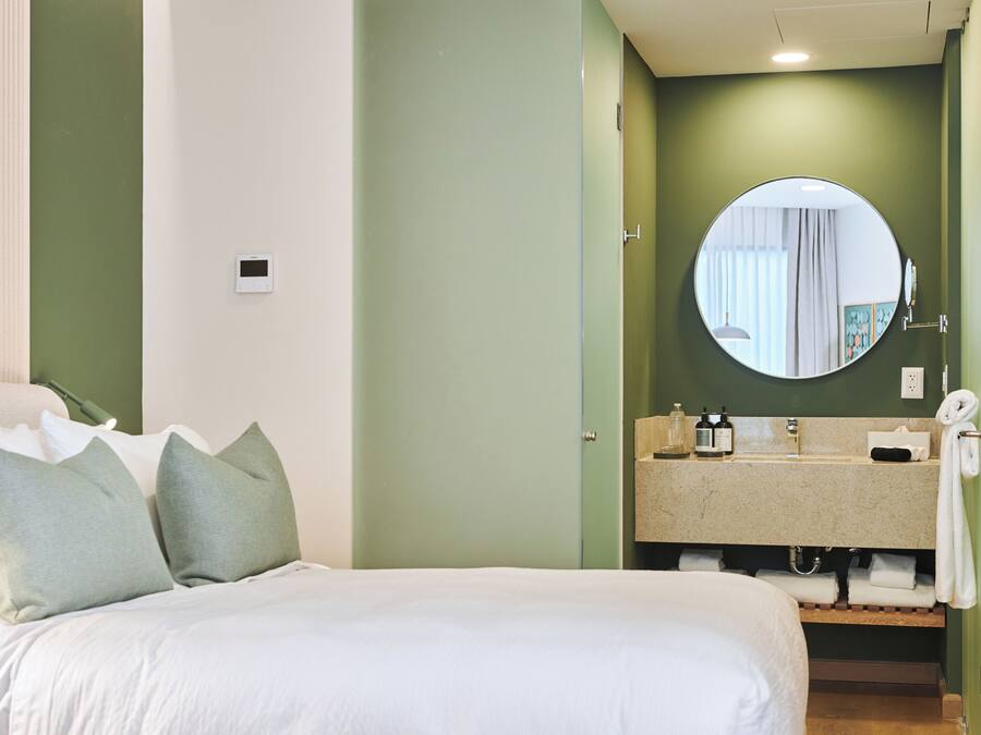 Une chambre d’hôtel avec un lit, des oreillers, un miroir rond, un lavabo et un porte-serviettes.