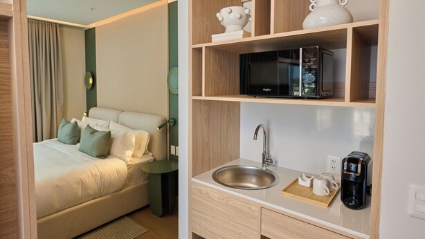 Ein modernes Hotelzimmer mit Bett, Nachttisch, eingebauter Mikrowelle, Spüle und Kaffeemaschine.
