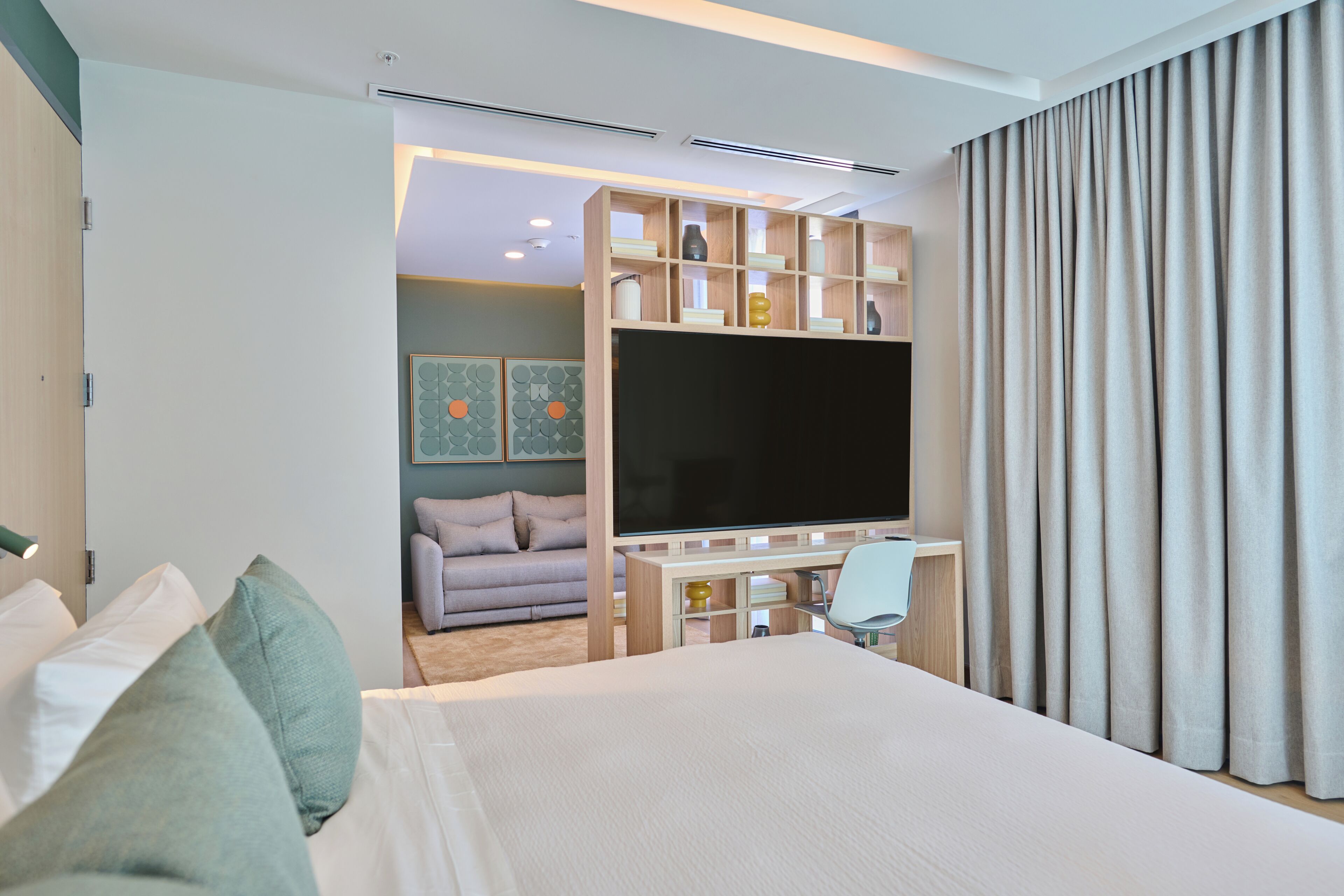 Une chambre d’hôtel moderne dotée d’un grand lit, d’une télévision, d’un bureau et d’un coin salon avec un canapé et des fauteuils.