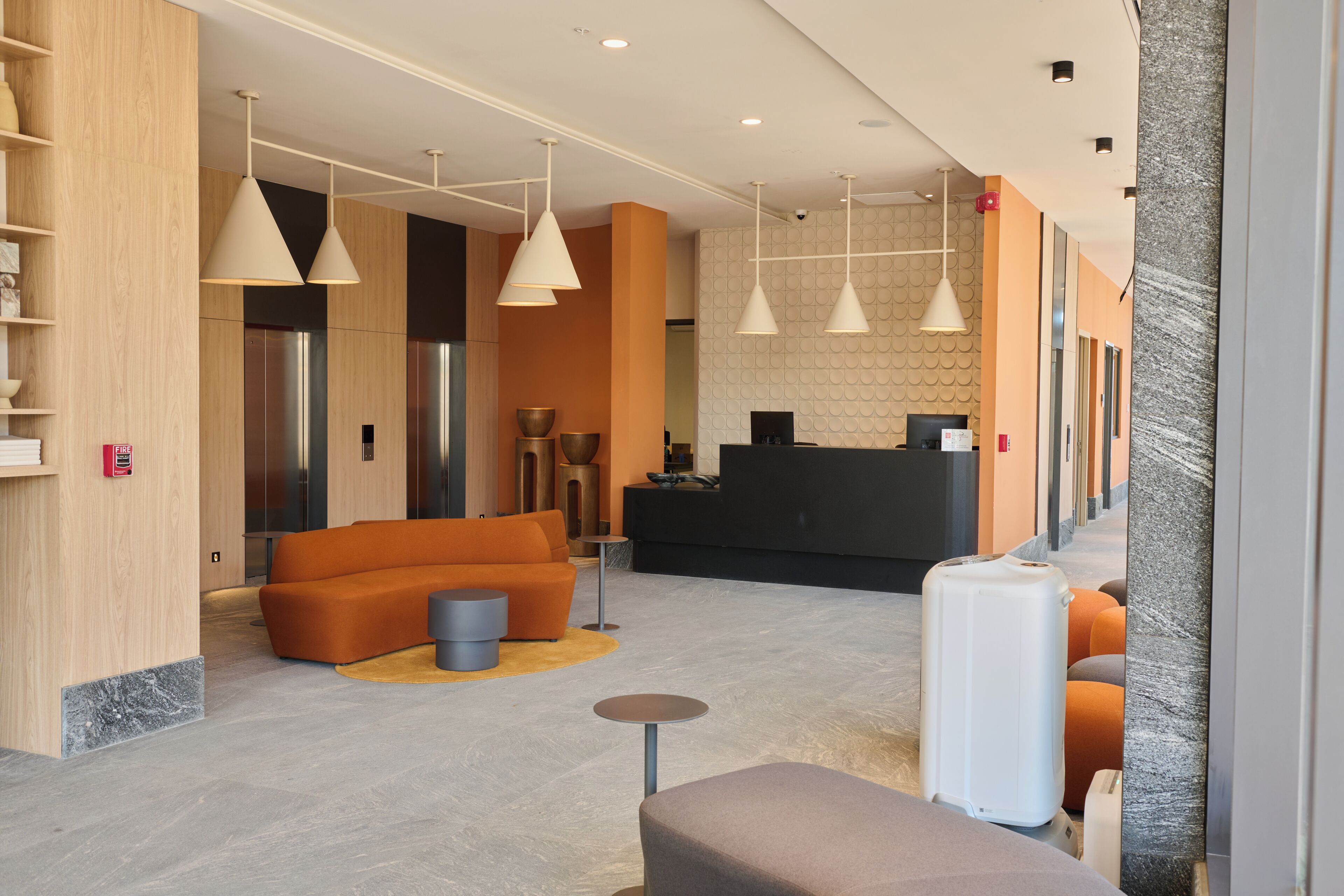 A modern lobby with a reception desk, orange seating, and pendant lighting.