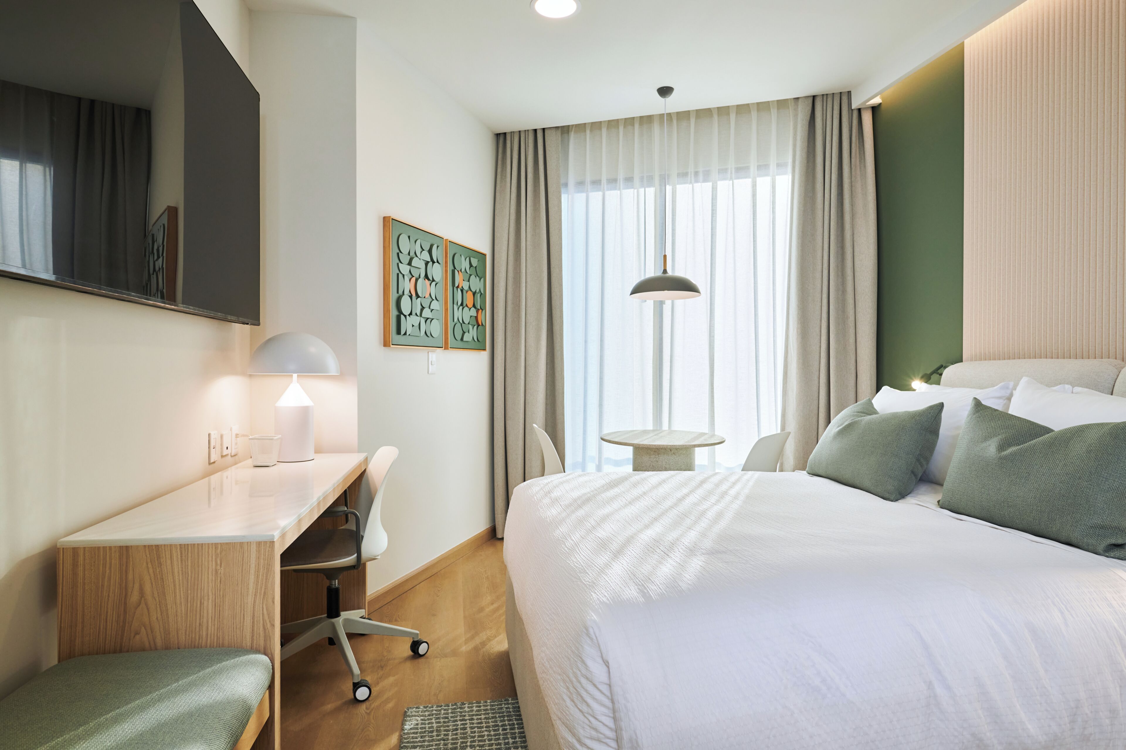 A hotel room with a bed, desk, chair, and a large window with curtains.
