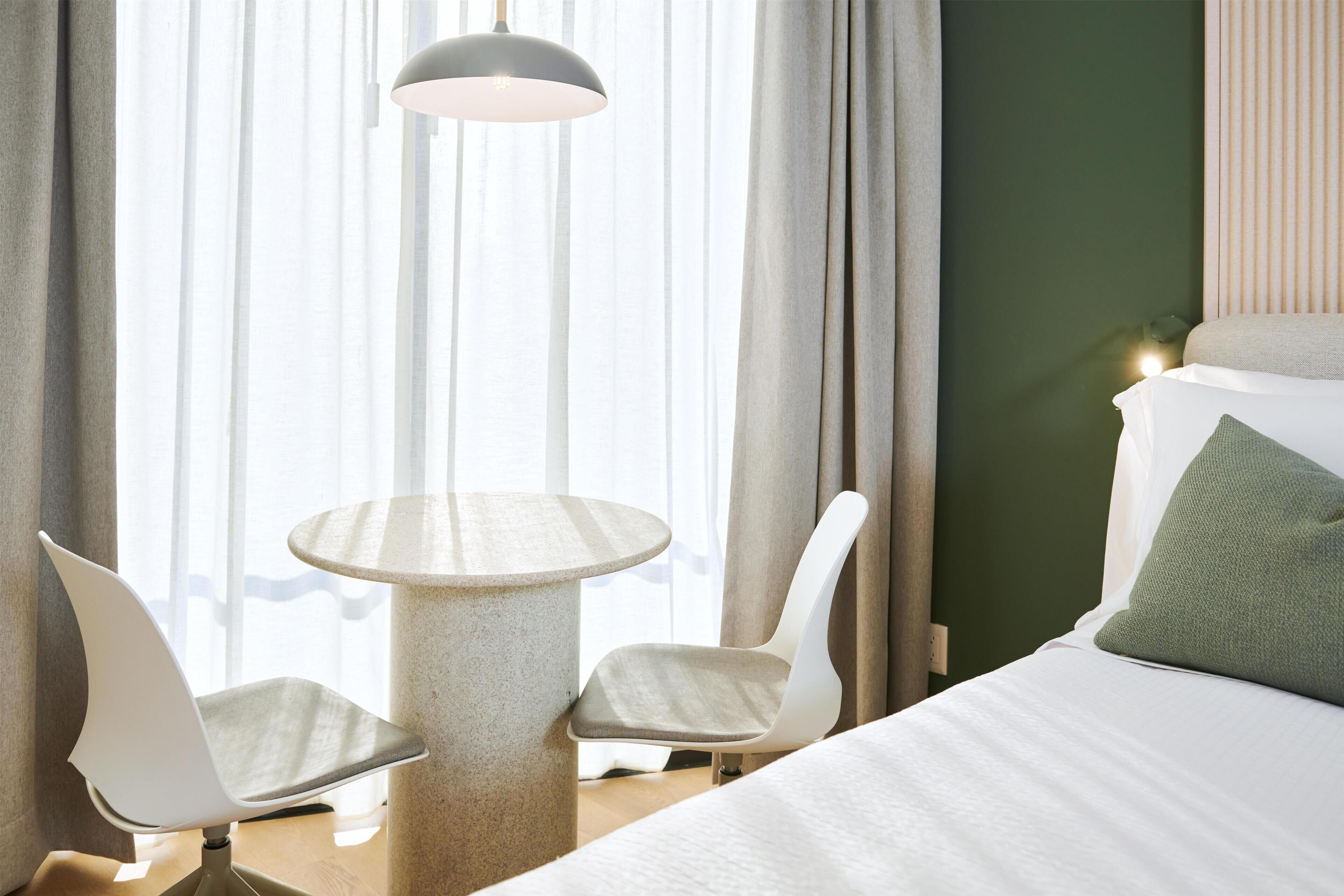 Une chambre d’hôtel avec un lit, deux chaises, une petite table et une lampe.
