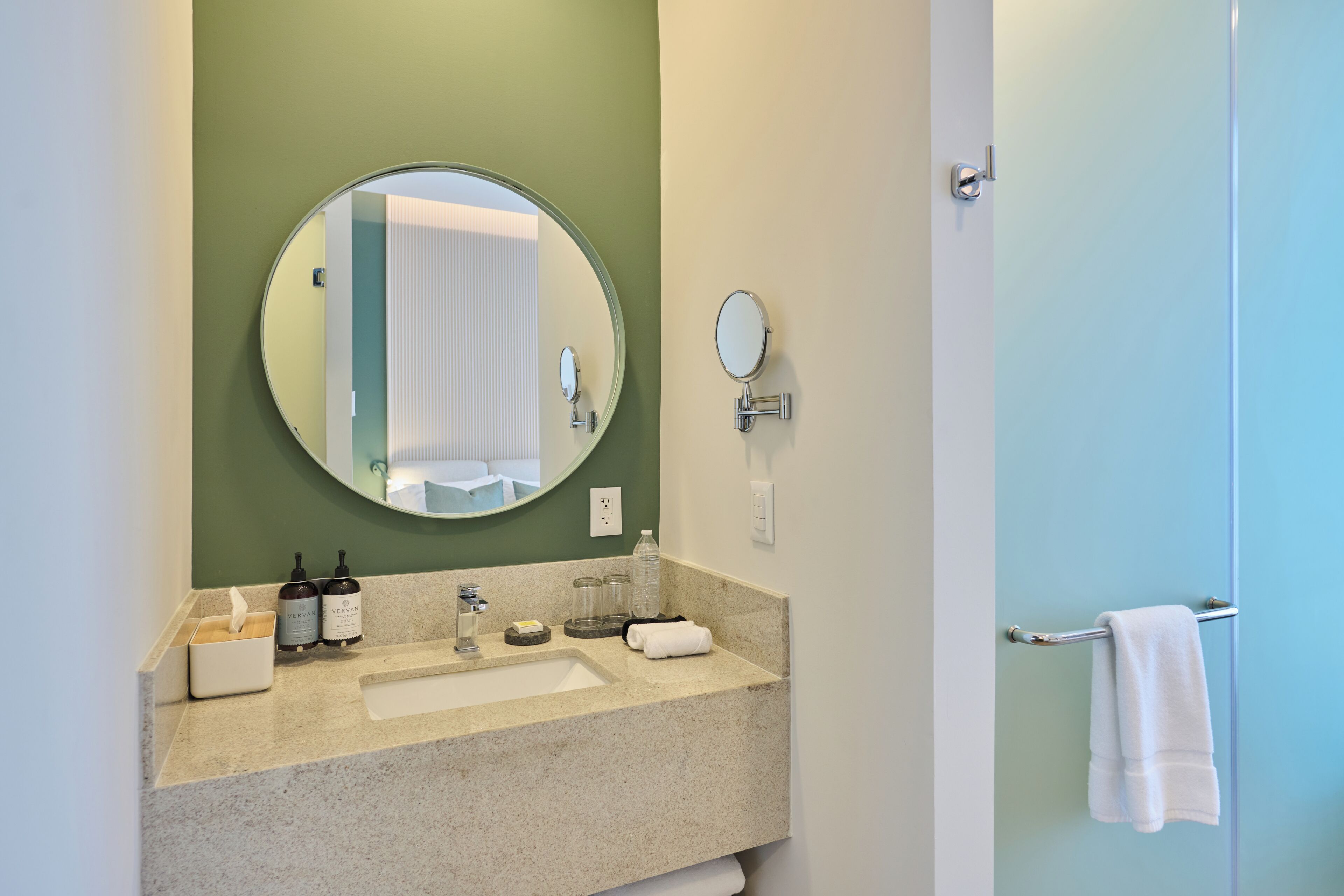 A bathroom with a sink, mirror, towel rack, and toiletries.