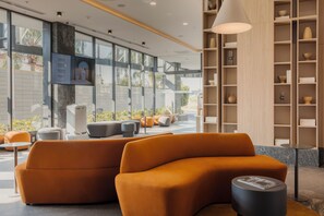 A modern lobby with orange seating, a large window, and a bookshelf with decorative items. - WorldHotels Guadalajara Zona Andares (Zapopan)