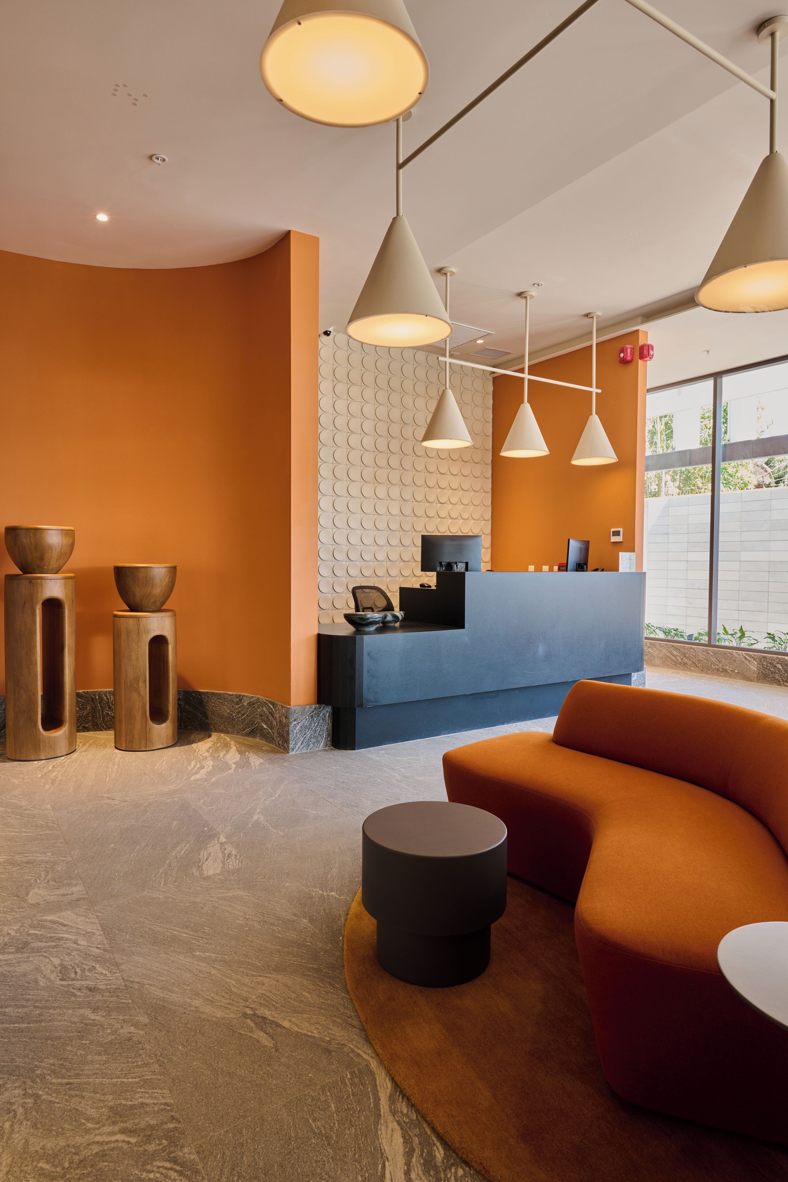 A reception area with a blue counter, three pendant lights, and a seating area with an orange sofa and a round table.