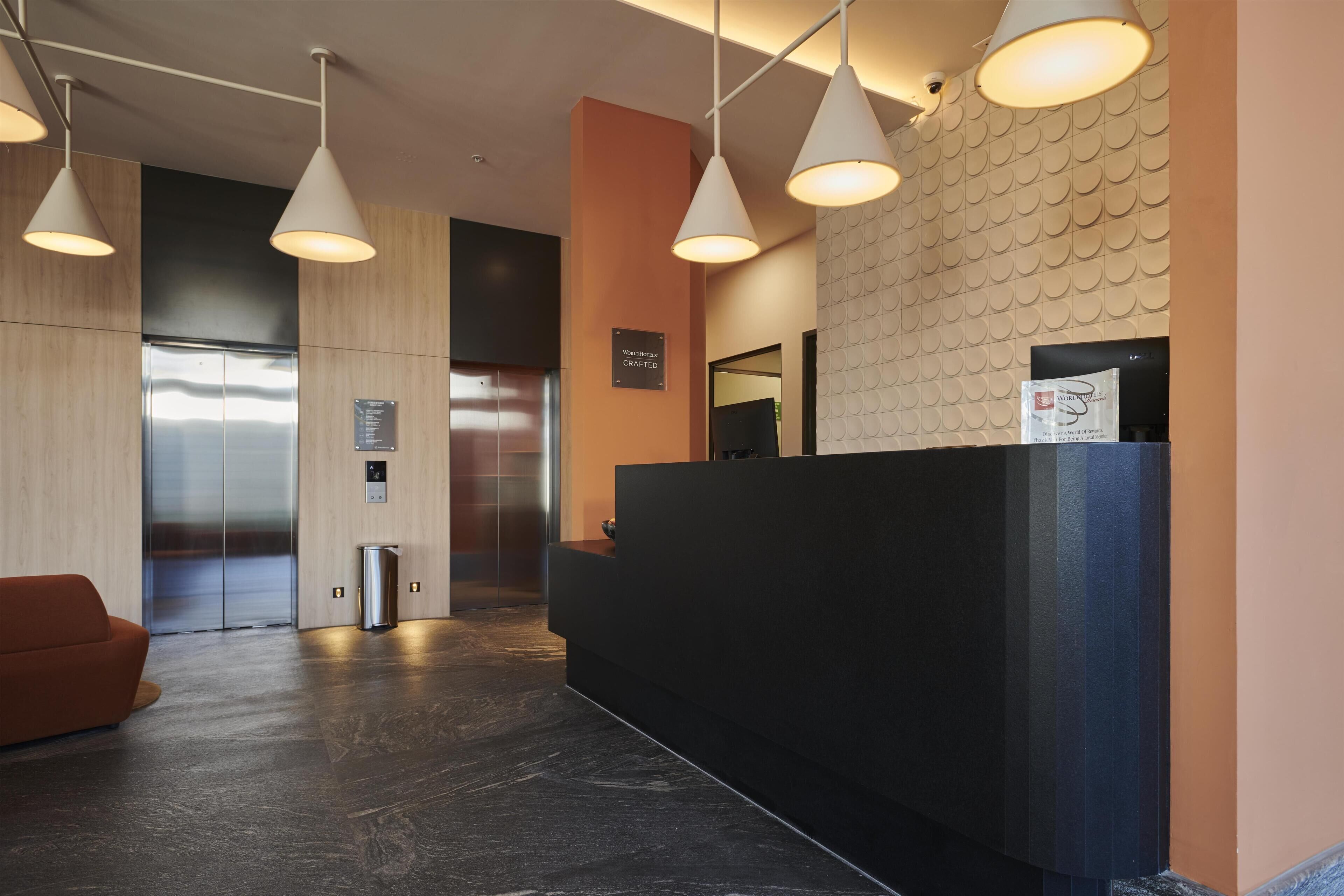 A modern reception area with a black reception desk, two elevators, and a seating area with a brown sofa.